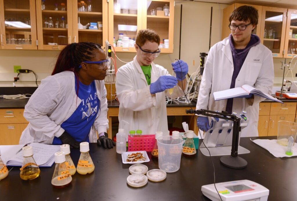 Three students in lab coats looking at a liquid in a beaker