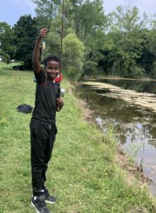 Boy holding up a fish he caught in a pond nearby